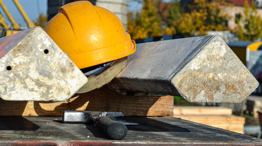 Ein Bauhelm und ein Hammer liegen zwischen zwei Stahlträgern