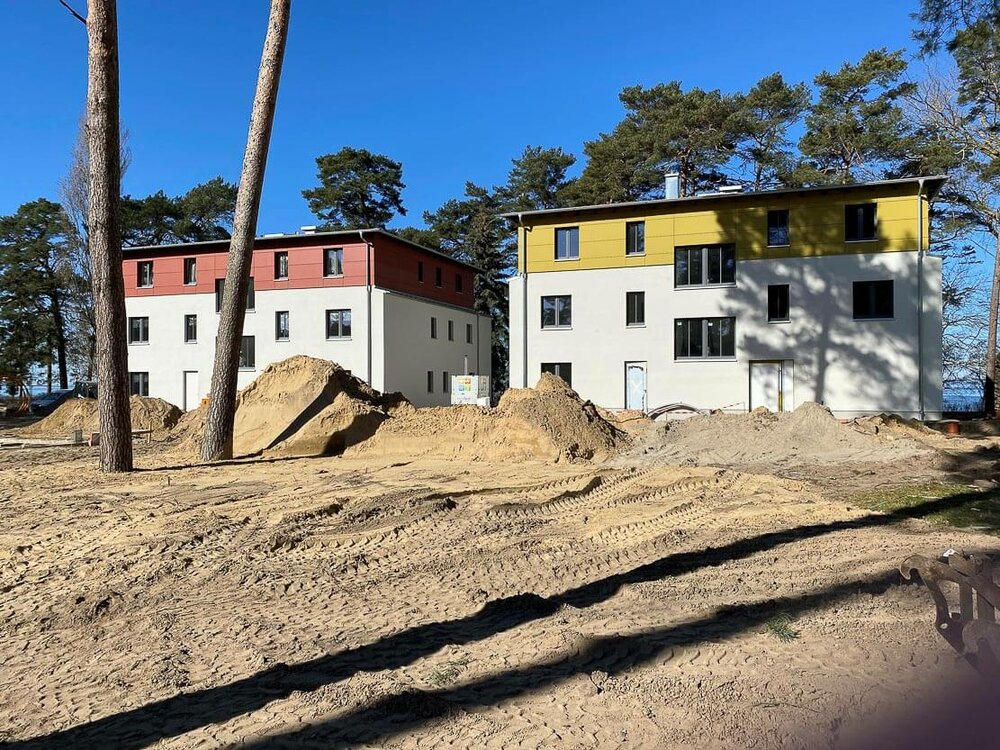 Im Hintergrund zu einer großen Sandfläche stehen zwei Neubauten