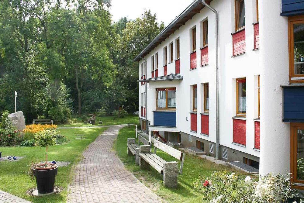 Ein Fußweg führt entlang eines weißen Gebäudes mit bunten Fensterrahmen und 