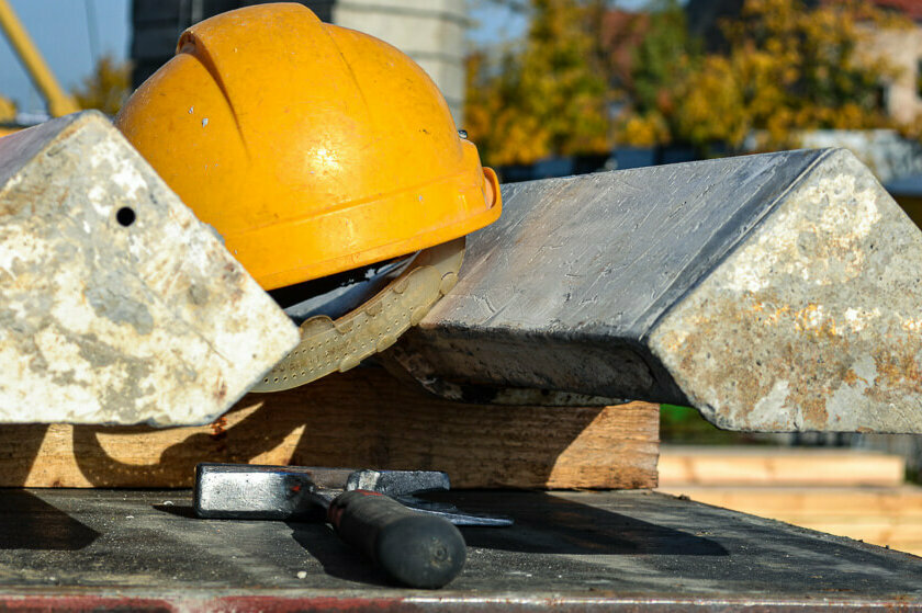 Ein Bauhelm und ein Hammer liegen zwischen zwei Stahlträgern