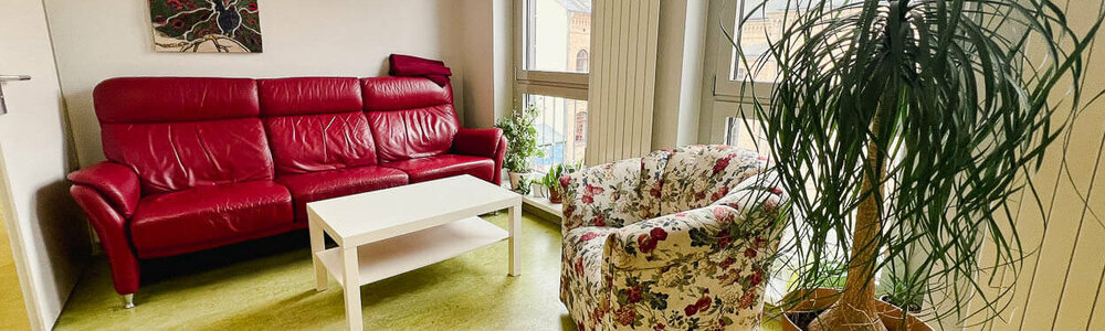 Eine Sitzecke mit Sofa, Couchtisch und Sessel und einer Pflanze in der Tagesstätte Steg Greifswald